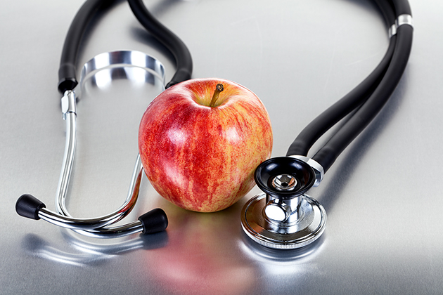 Red apple with stethoscope on stainless steel table with reflection. Good health concept.