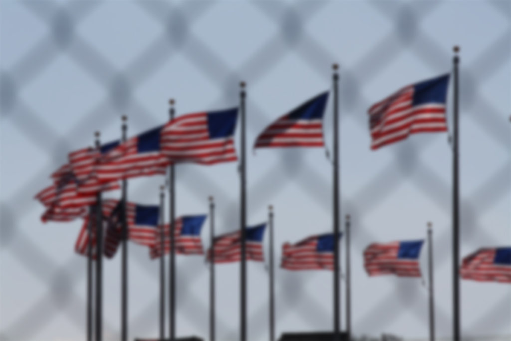 blurredAmericanflagsbehindchainlinkfence Texas Catholic Conference